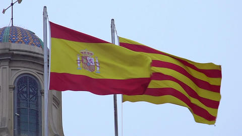 Spanish and Catalan flags with coat of arms fluttering in wind against blue sky