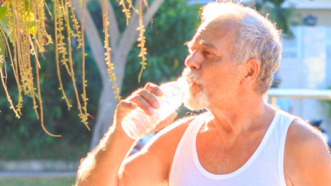 Old Man Drinks Water during Morning Exercises in Park