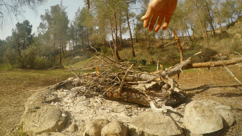 POV Hands throwing firewood in a smoking fire near the forest on a bright day