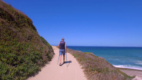 Man Uses Sticks for Scandinavian Walking on the Beautiful Sea Shore