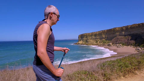 Man Uses Sticks for Scandinavian Walking on the Beautiful Sea Shore