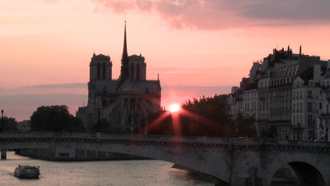 A boat floating past Notre Dame as the sun sets in the background