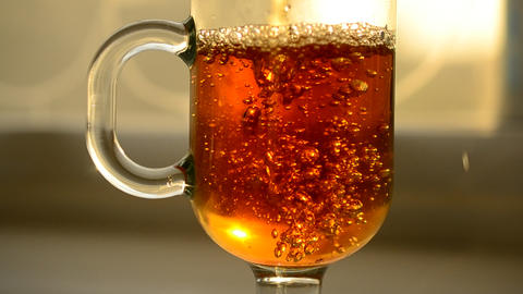 Pouring black tea into empty glass cup with bubbles and foam