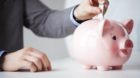 close up of man putting money into piggy bank