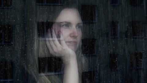 Sad and thoughtful young woman. Looking out through a window