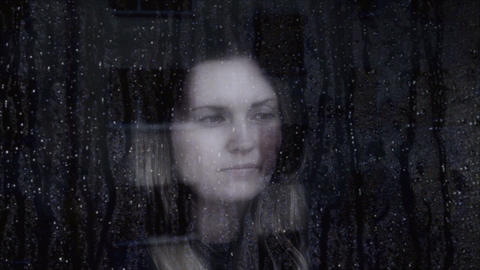 Sad and thoughtful young woman looking through a window