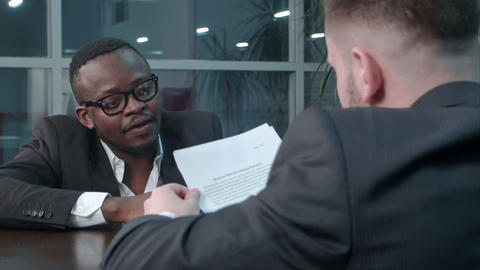 Interracial businessmen shaking hands in business hall, smiling