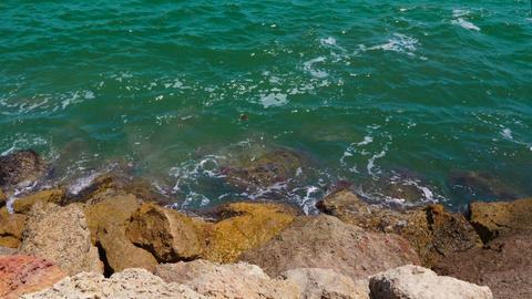 Green waves splashing on rocks on seacoast, close up