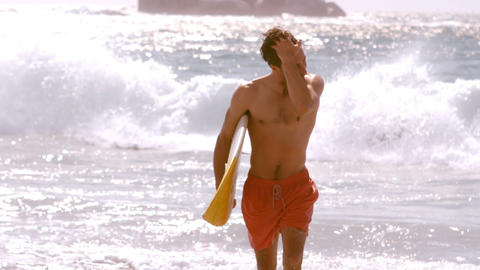 A man is touching his hair and he is returning on the beach