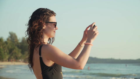 Happy woman takes pictures of sunset over sea