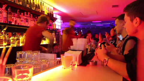 Low frame rate shot of bar in club. Two bartenders serve drinks for visitors