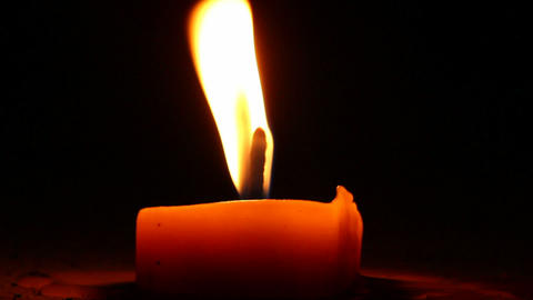 Burning candle in the night. Wind blows and flame shimmers