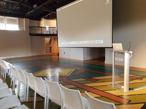 Chairs seated in front of podium with projector screen and colored tiles