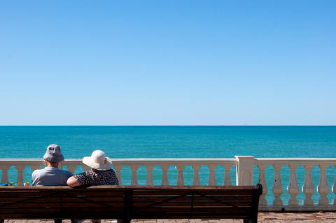 a couple of adults sits on the promenade and looks out at the sea