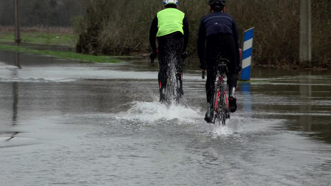 Cyclists riding on a flooded road, Water over road, Road flooded by the overflow