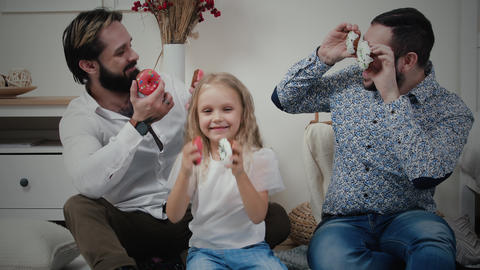 Male couple and little girl having fun with donuts