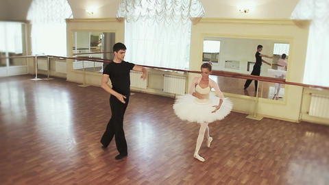 Graceful couple dancing ballet simultaneously in front of mirror