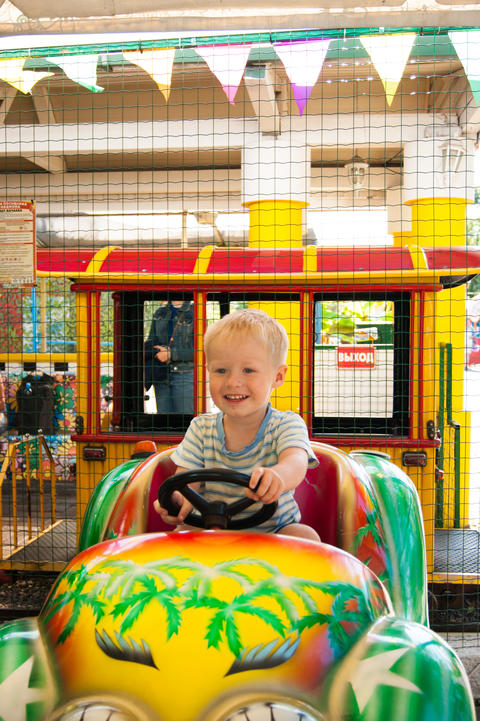 A very joyful and happy little blond boy of three years old is riding in a