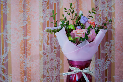 A delicate bouquet of different flowers in a light pink wrapper stands against a
