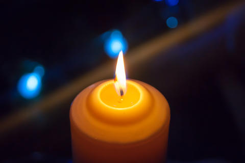 A burning orange candle on a dark background with blue lights - a Christmas New