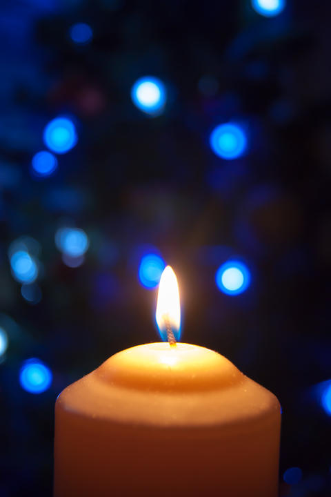 A large candle burns against the background of a garland with shining lights