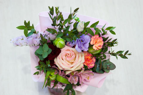 A delicate bouquet of different flowers in a light pink wrapper stands on a