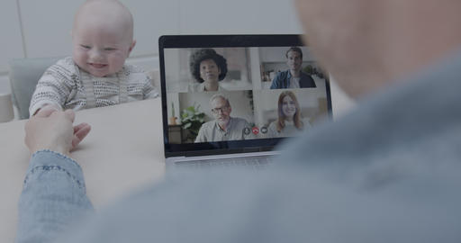 Father on video call in kitchen with colleagues and looking after baby, using Video Conferencing