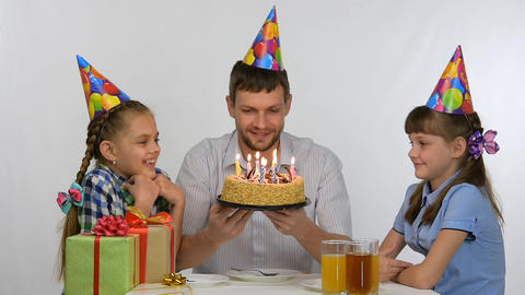 Children kiss dad who sits at a table with a festive cake