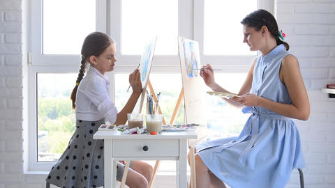 Mom and daughter paint at home in front of the window on easels