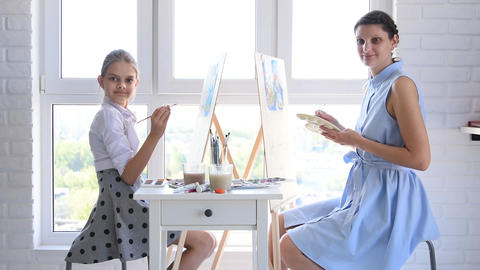 Mom and daughter paint at home in front of the window on easels and looked into the frame
