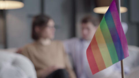 Focus changes from rainbow lgbt flag to gay couple chatting at the background