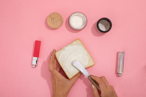 Hands smear cosmetic cream on bread