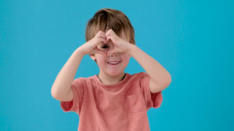 Kid makes heart with fingers posing for camera on turquoise