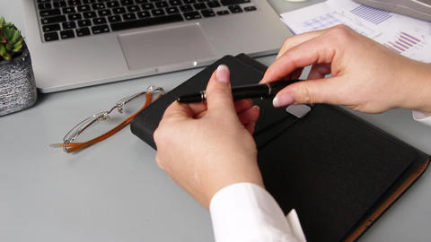 Business woman hands closing a pen near agenda and laptop close up