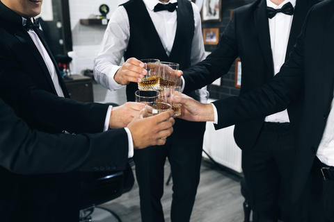 Promising young men celebrate and drink whiskey. Best men with glasses filled up