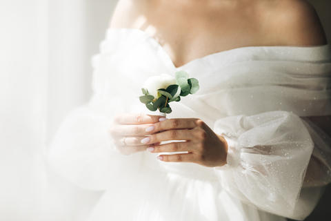 Close-up of the bride's hands holds a boutonniere. Woman in a beautiful white
