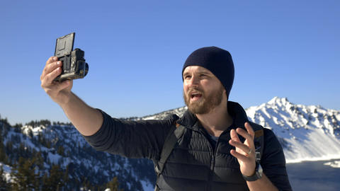 Man recording himself with snowy mountain range and blue sky as background