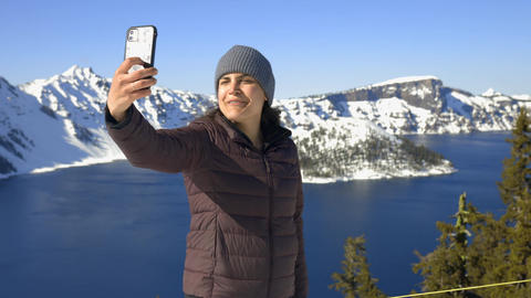 Woman recording herself phone selfie snowy Crater Lake, Oregon as background