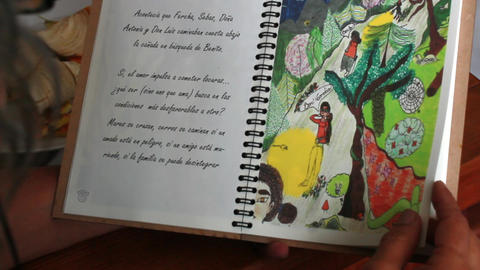 Hands holding open spiral book with drawings from behind long gray hair