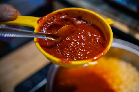 Red chili pepper paste in plastic strainer above cooking pot