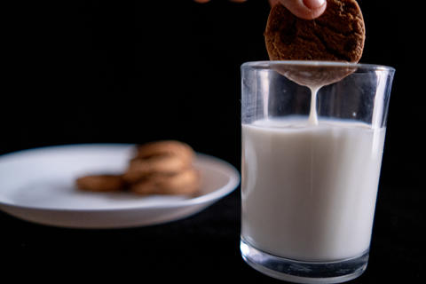 Hand dunking a cookie in glass of milk with black background