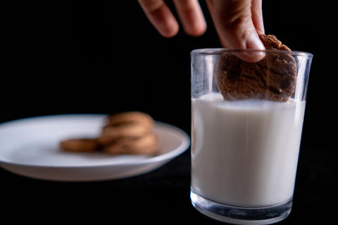 Hand dunking a cookie in glass of milk with black background