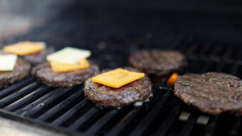 Hamburger meat with cheese slices above iron barbecue grill