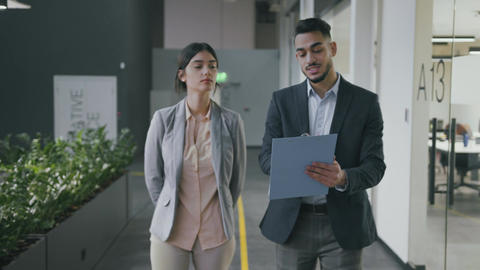 Young arab businessman walking with woman investor along office and showing her