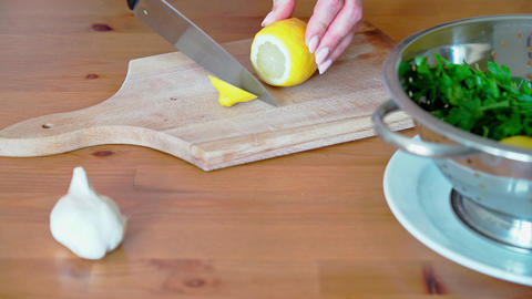 female hands with a knife cutting lemon on a wooden cutting board