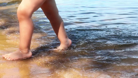 Unrecognizable baby girl walks in water, slow motion