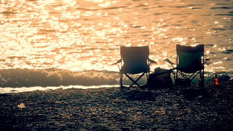 Silhouettes of two empty folding camping chairs set on a pebble beach for