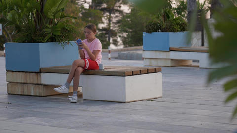 Teenage girl sits on a bench posting in social media apps, chatting with friends