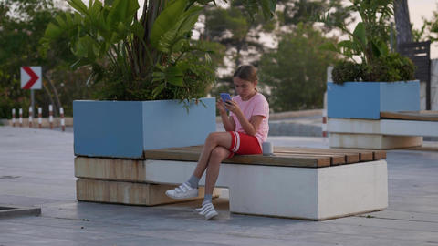 Teenage girl sits on a bench posting in social media apps, chatting with friends