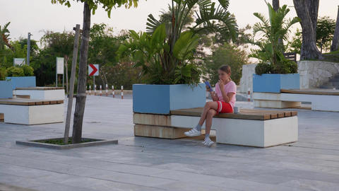 Teenage girl sits on a bench posting in social media apps, chatting with friends